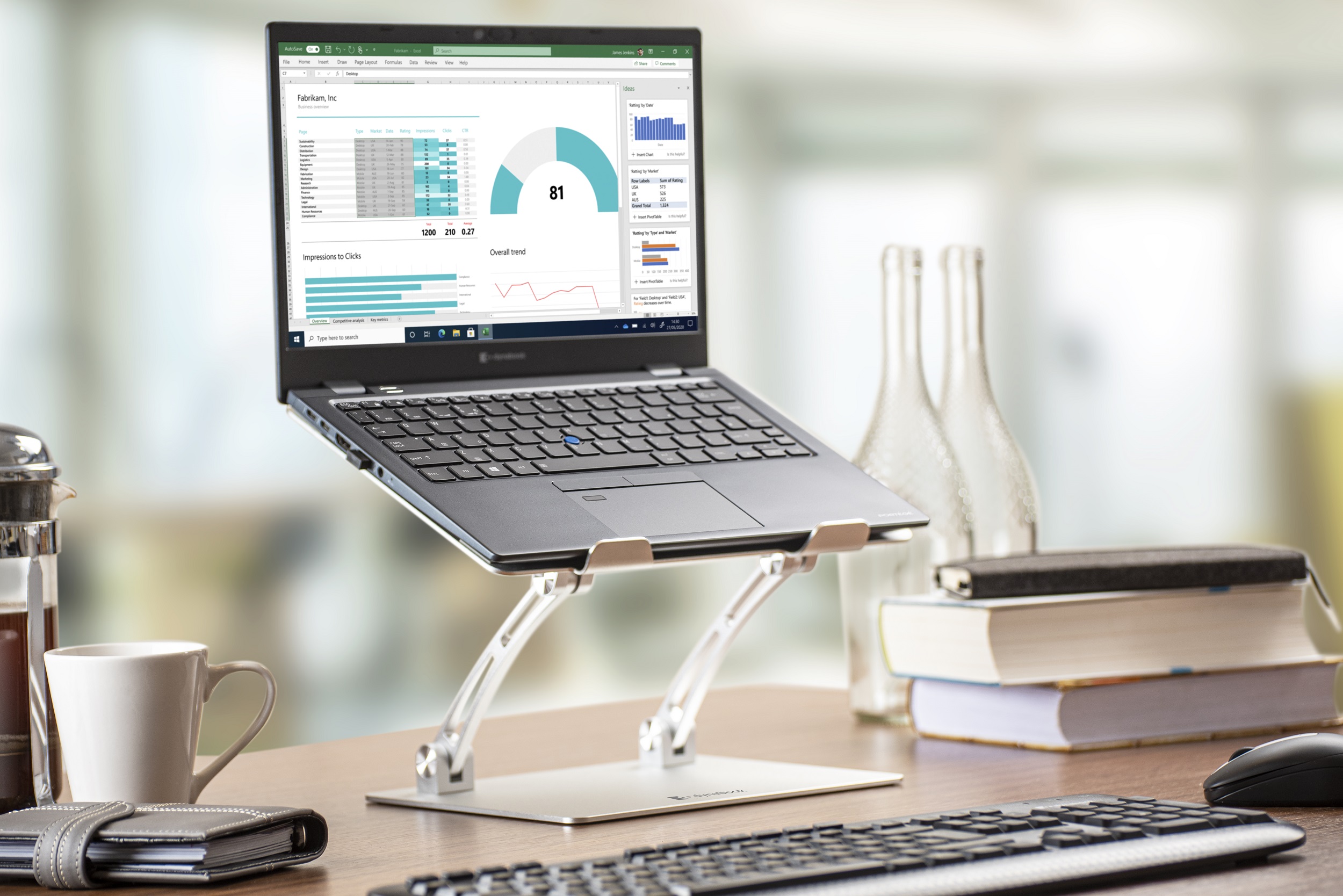 Zu sehen ist ein Notebook, dass auf einem erhöhten Standfuß auf einem Schreibtisch steht. Der Standfuß ermöglicht einen komfortablen Blick auf das Notebook für den Nutzer.